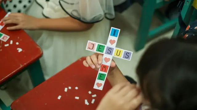 Child holding a paper Jesus cross craft at a Sunday school table