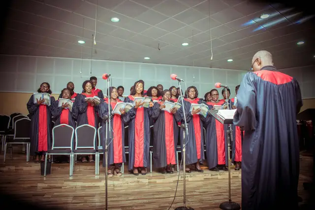 Nigerian church choir in red and black robes standing in rows with their conductor
