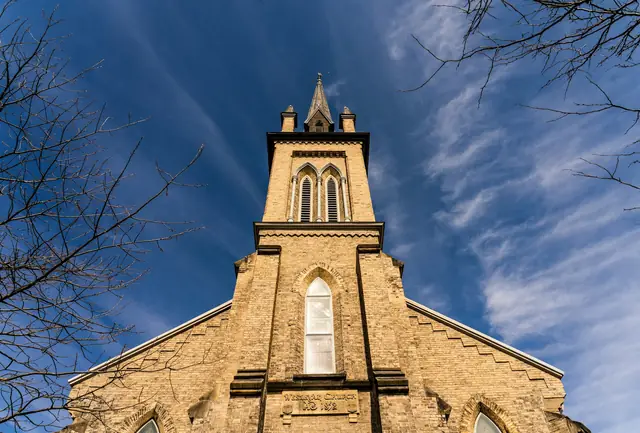 Stone church with a tall gothic tower under a blue sky with wispy clouds