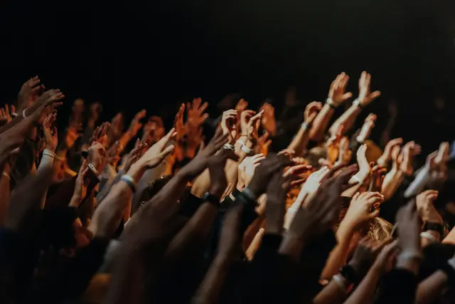 Silhouetted crowd of worshippers with raised hands in warm stage light