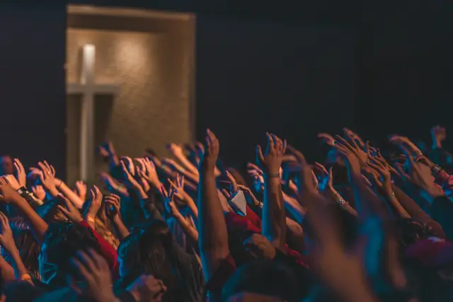 Congregation raising their hands in worship in front of a stage with a cross