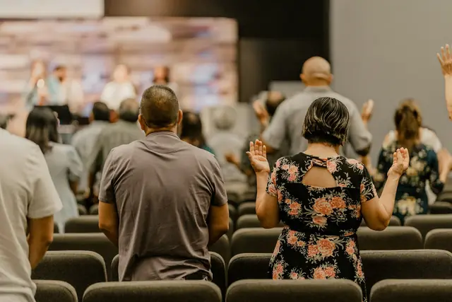 Congregation seen from behind, standing with hands lifted in praise