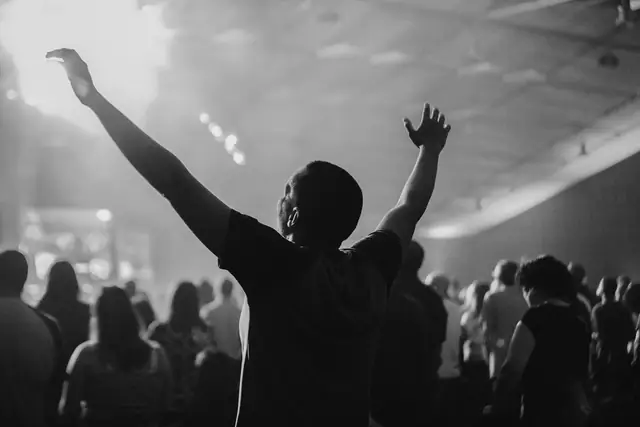 Black and white photo of a person with arms raised in a worshipping crowd